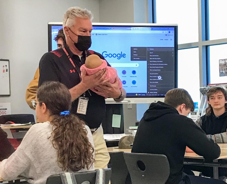 Coach Brad Crawford babysits for a student while teaching. Students in Child Development class had the option to carry a flour sack baby or robot baby this week.