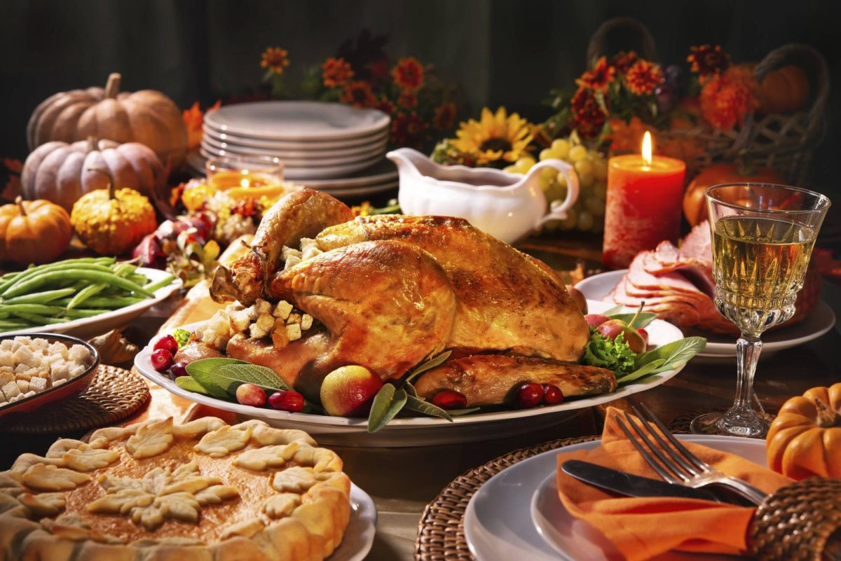 Thanksgiving dinner. Roasted turkey garnished with cranberries on a rustic style table decoraded with pumpkins, vegetables, pie, flowers, and candles.